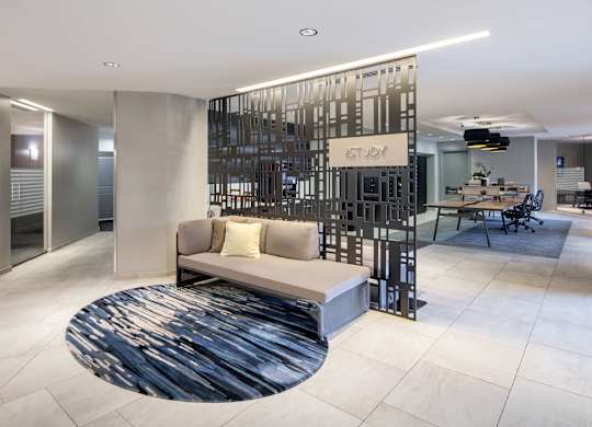 Vantage Mosaic lobby study area with a gray bench, round rug, black decorative partition and communal table beyond.