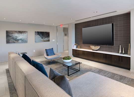 Resident lounge with a gray sectional facing a wall-mounted television and long media console.