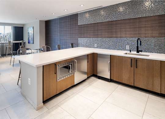 Close view of the resident lounge kitchen with wood cabinets, white countertops, sink, beverage refrigerator and large island.