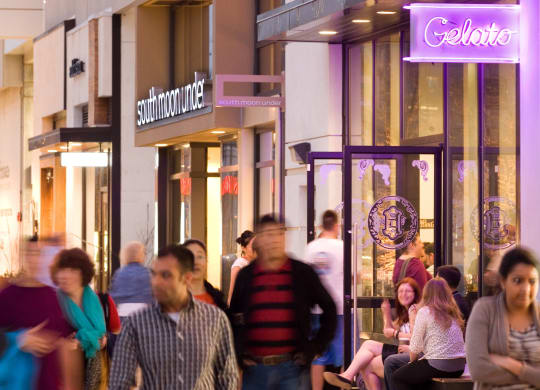 people walking down a city street at night in front of shops