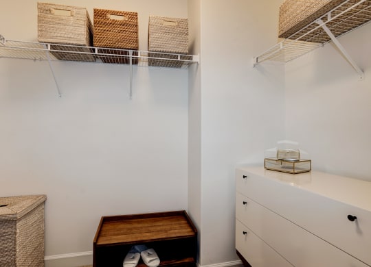 a walk in closet with white walls and shelves and a white dresser with baskets
