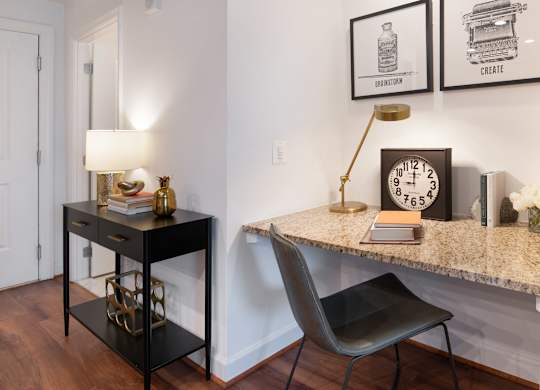 Built-in granite desk in a model apartment with a gray chair, brass task lamp, framed artwork and decorative accessories.