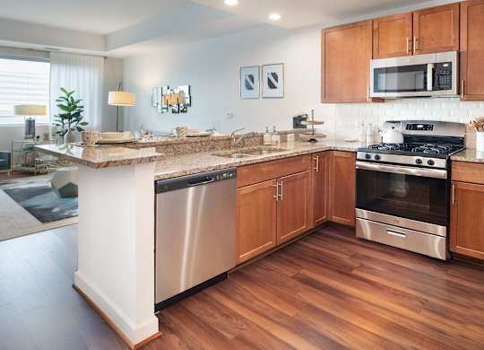 Open model kitchen with granite counters, wood cabinets, stainless steel appliances, gas range and hardwood flooring.