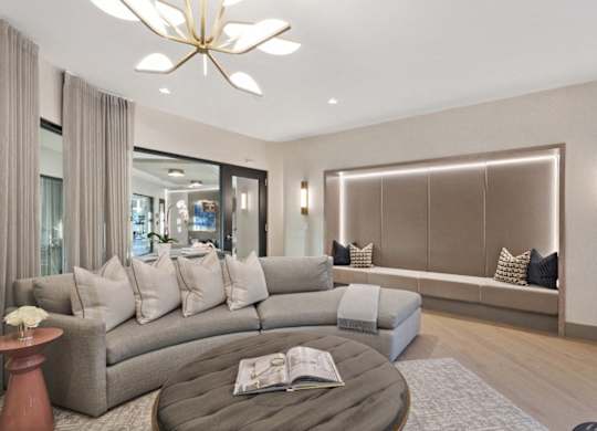 A living room with a grey sofa, a round table with a book on it, and a chandelier hanging from the ceiling.