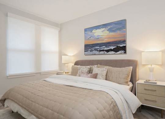 A bedroom with a large bed, a nightstand with a lamp, and a painting on the wall.