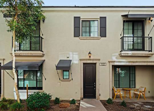 A beige building with black doors and windows has a small patio with a table and chairs.