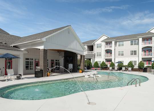 A swimming pool in front of a building with a red umbrella and white chairs. at Concord Ridge Apartments, North Carolina