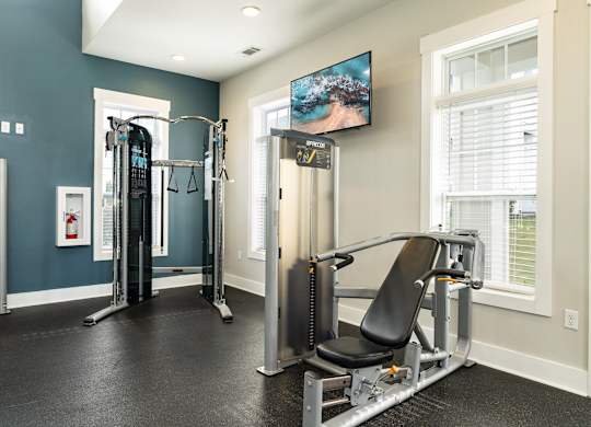 A home gym with a variety of equipment including a treadmill, a weight machine, and a television. at Concord Ridge Apartments, Concord, North Carolina