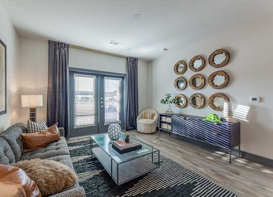 A living room with a grey couch, a glass coffee table, and a large painting on the wall. at Magnolia Grove Apartments, Texas