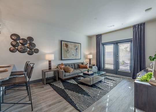 A modern living room with a grey sofa, a glass coffee table, and a large abstract painting on the wall. at Magnolia Grove Apartments, Terrell, Texas
