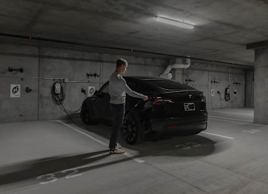 A man is charging an electric car in a parking garage.