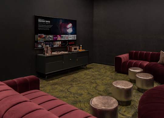 A room with a red couch and ottoman in front of a black wall with a poster on it.