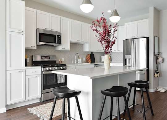 a kitchen with white cabinets and a white island with black stools at The Hallon Apartments, Hopkins, Minnesota