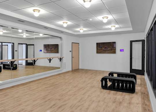 A dance studio with a mirrored wall and wooden flooring.