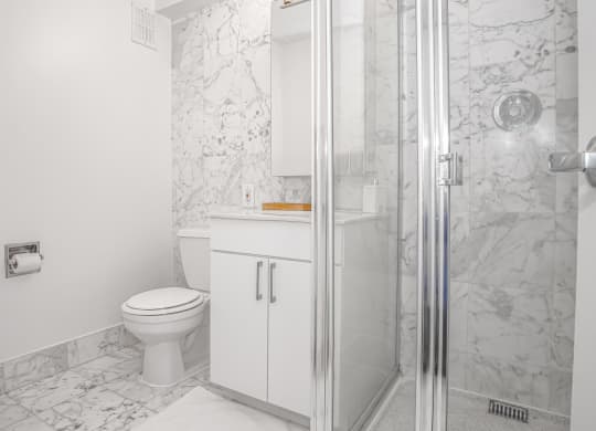A bathroom with white cabinet and toilet and marble walls