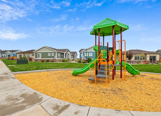 a playground with yellow mulch and houses in the background