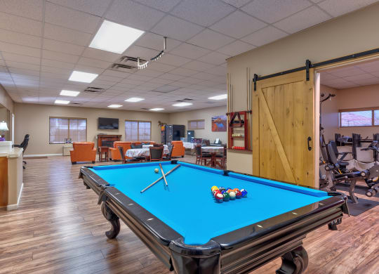 a pool table in the clubhouse of a community center with a gym and exercise equipment