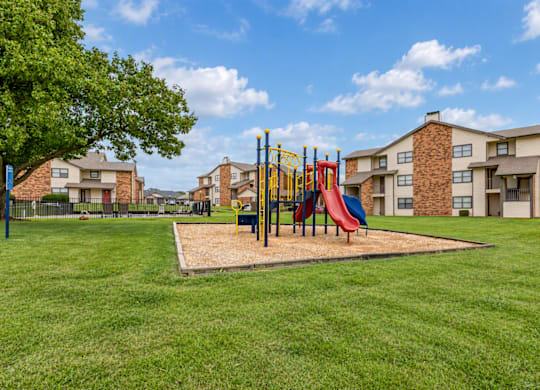 A playground with a red slide and a yellow swing set in a grassy area.