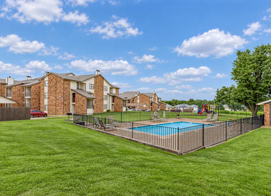 A large grassy area with a pool and apartment buildings in the background.