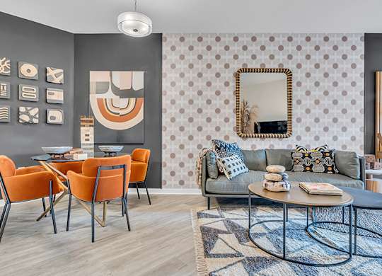 A living room with a grey couch, orange chairs, and a patterned wallpaper.
