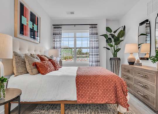 A bedroom with a large bed, a window with curtains, and a painting on the wall.