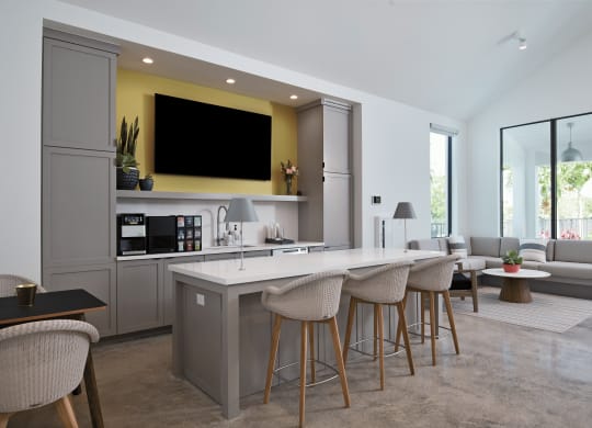 a kitchen and living room with a large white island with stools and a yellow accent wall