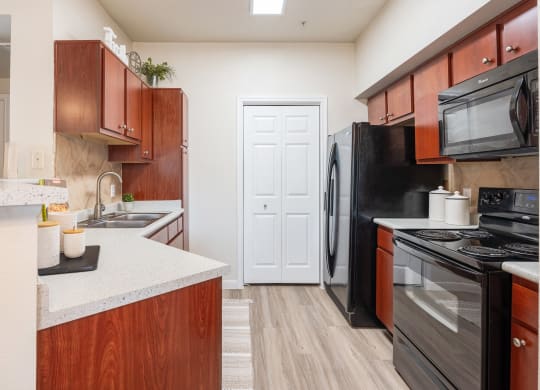 Kitchen with black appliances and wood cabinets at Park Hudson Place Apartments, Bryan, Texas