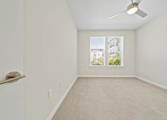 A room with a ceiling fan and a window with a view of a building.