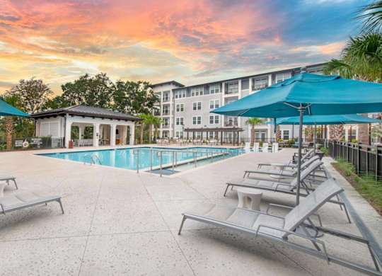 A pool area with sun loungers and a building in the background.