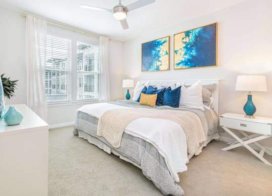 A bedroom with a bed, a ceiling fan, and a painting on the wall.