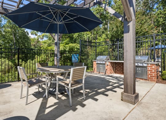 a grilling patio with a table and chairs under an umbrella