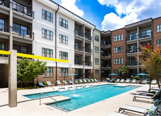 a swimming pool with lounge chairs in front of an apartment building