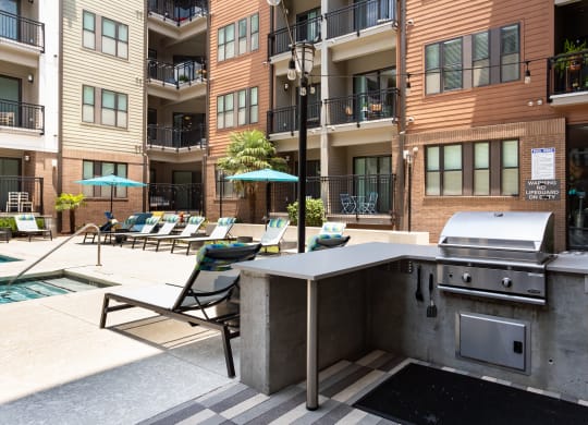 an outdoor kitchen with a grill and lounge chairs in front of an apartment building