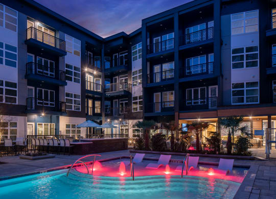 an apartment building with a pool and chairs at night