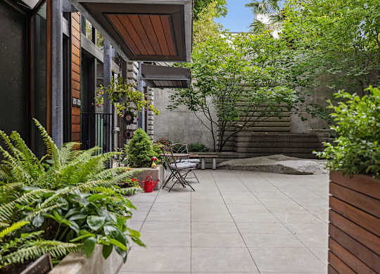 A patio with a table and chairs surrounded by green plants.