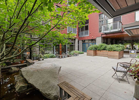A patio with a bench and a tree in front of a building.