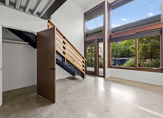 A room with a wooden door and a window with a view of trees and a car outside.