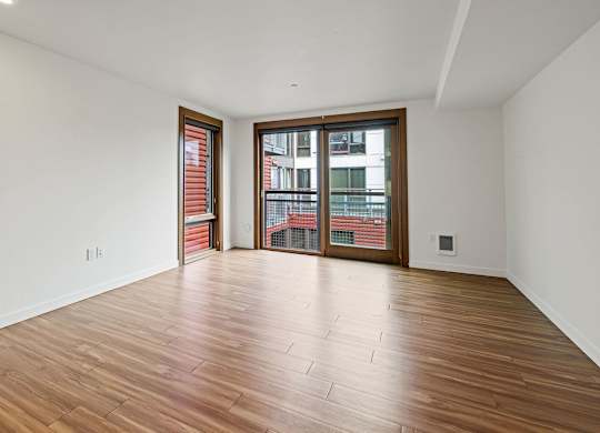 A room with wooden flooring and a large window with a view of a cityscape.