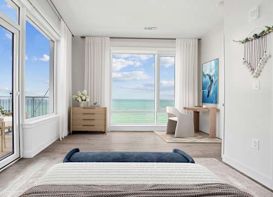 Penthouse bedroom with a sliding door out to the balcony, a desk by the window and open water filling the view.