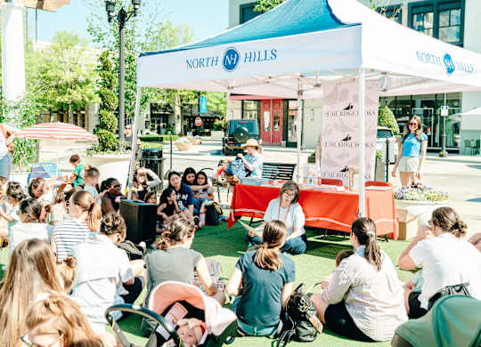 A group of people are sitting on the grass in front of a tent with the sign