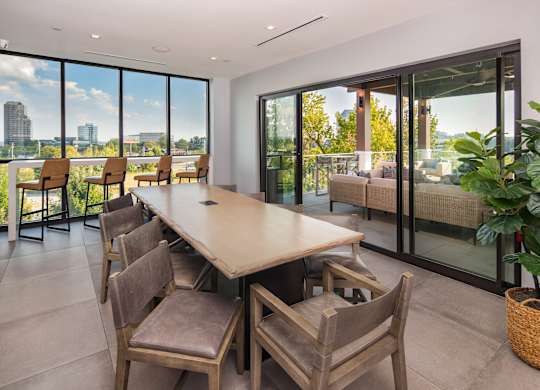 A long table with chairs is in a room with a view of the city.