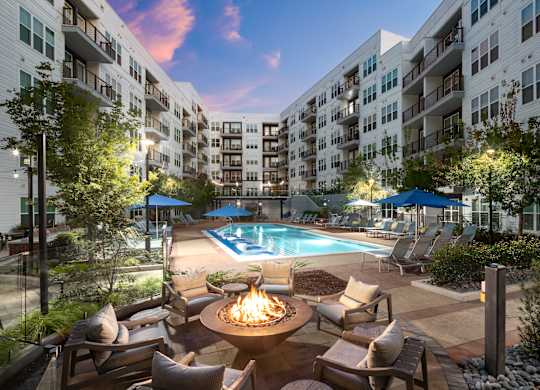 A pool surrounded by chairs and a fire pit in the middle of a courtyard.