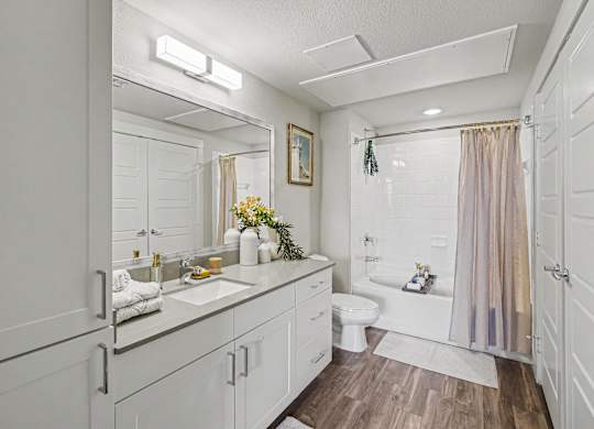 Bathroom with a white vanity, gray counter, wide mirror, a tall linen cabinet, and a tub and shower with white subway tile.