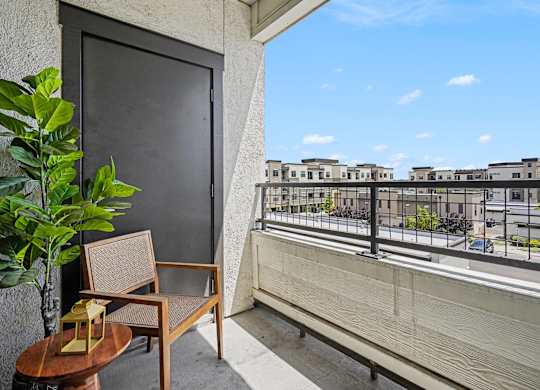 Covered balcony with a cane-back chair, a round wood side table, and a metal railing overlooking neighboring buildings.