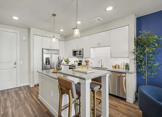White kitchen beside the front door, with a stainless refrigerator, dishwasher, and microwave and a two-stool island.