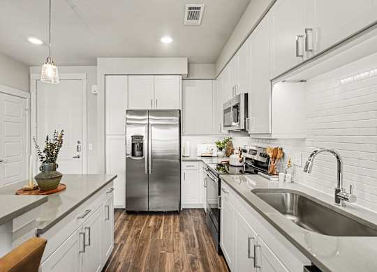 Kitchen with a stainless side-by-side refrigerator, white upper and lower cabinets, gray counters, and a subway tile wall.
