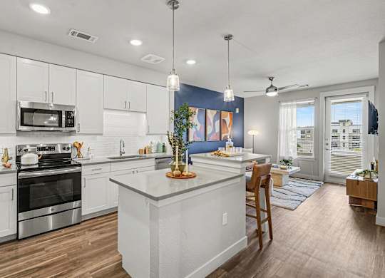 Kitchen with white shaker cabinets, subway tile backsplash, stainless range and microwave, and an island under two pendants.