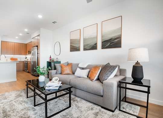 A modern living room with a grey couch, a black coffee table, and a large painting on the wall.