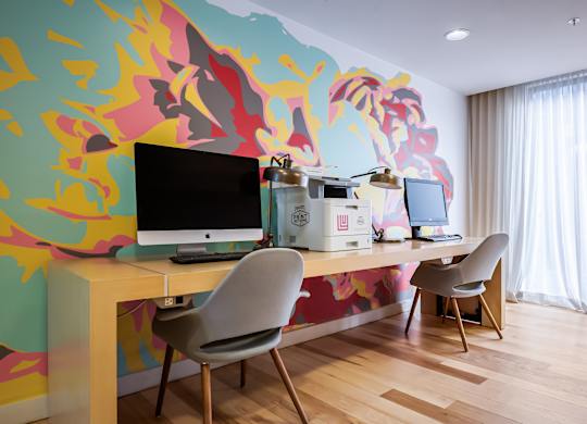 A room with a desk and chairs with a colorful wallpaper.