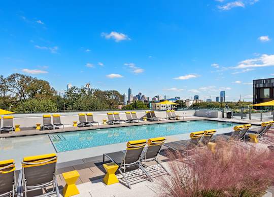 A pool with yellow chairs and a city view in the background.